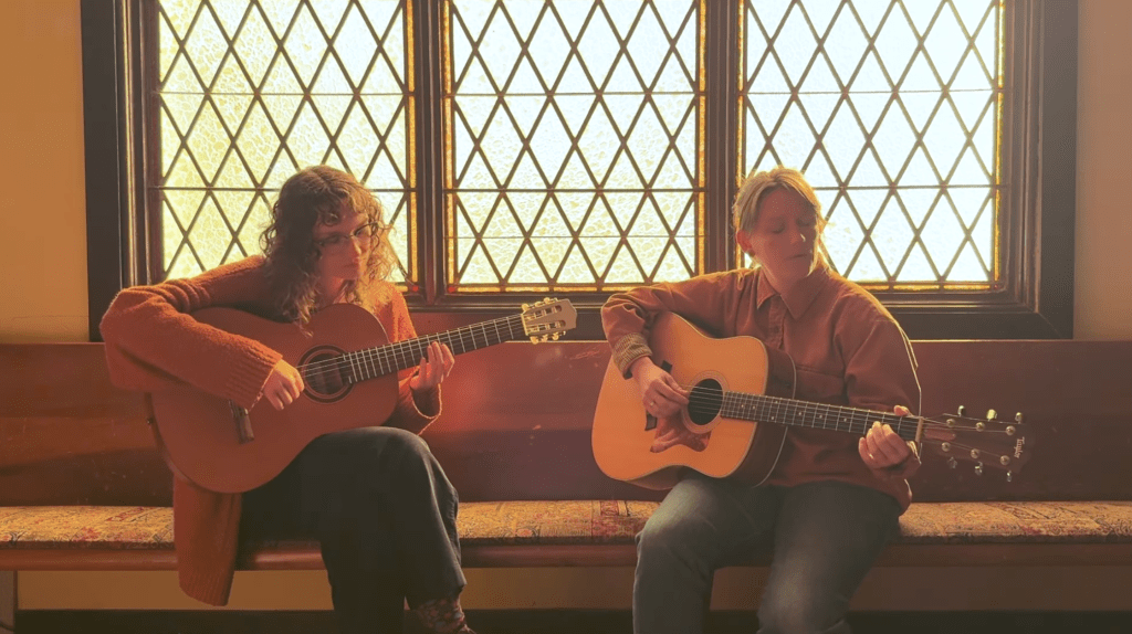 two musicians holding guitars in front of a stained glass window